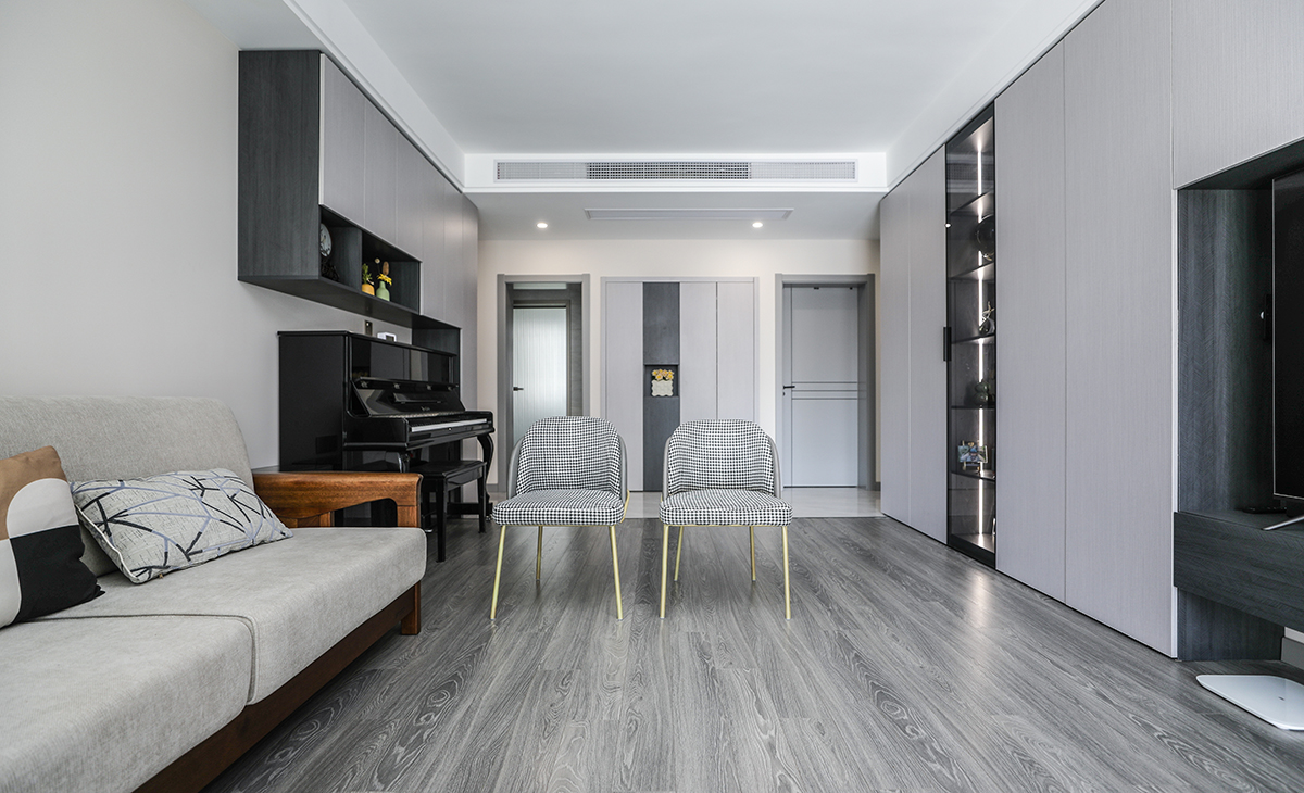 客廳開間很大，電視墻做一排裝飾柜，空間也很寬闊、裝飾柜采用淺灰色門板、淺灰和深灰相互配合，明暗有神，既能儲物又能裝飾、黑色的鋼琴上主做一排，黑白相配的吊柜，原木色沙發框架+淺灰色座墊讓客廳的氛圍年輕起來了。吊頂造型上采用雙眼皮吊頂。地面采用灰色地板。造型和色調上無不給人以簡潔、大氣、時尚的感覺。