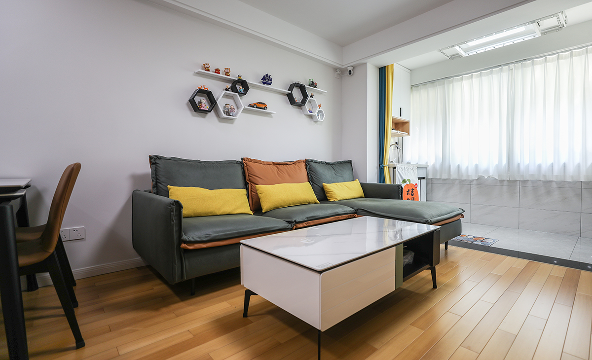 沙淺灰色沙發框架+橙色座墊讓客廳的氛圍年輕起來了，沙發背景墻黑白配層板裝飾，代替傳統的壁畫，使空間上更加飽滿。