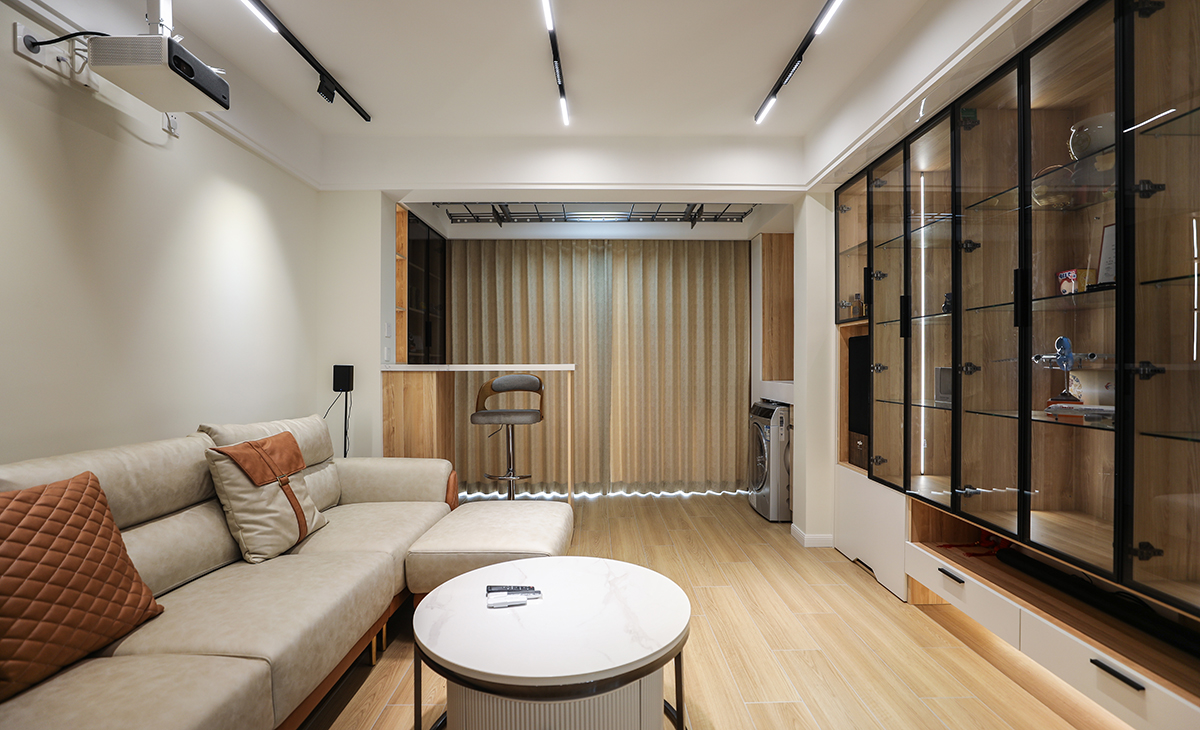 客廳是一家人活動頻率最高的區域，要求寬闊、明亮。沙發背景墻采用涂料，米色皮質沙發配白色方型茶幾加上原木色的地板磚，將客廳和陽臺連城一體，造型和色調上無不給人以簡潔、大氣、時尚的感覺。