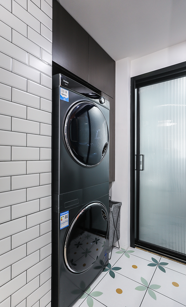白色黑線條墻磚，淡綠花色地磚讓干區空間上顯得開闊，洗衣機、烘干機鑲嵌在黑胡桃色雜物柜里，充分利用了空間，解決了敞開式陽臺沒有雜物柜的缺陷，也更襯托深綠色洗衣機的穩重、高冷。