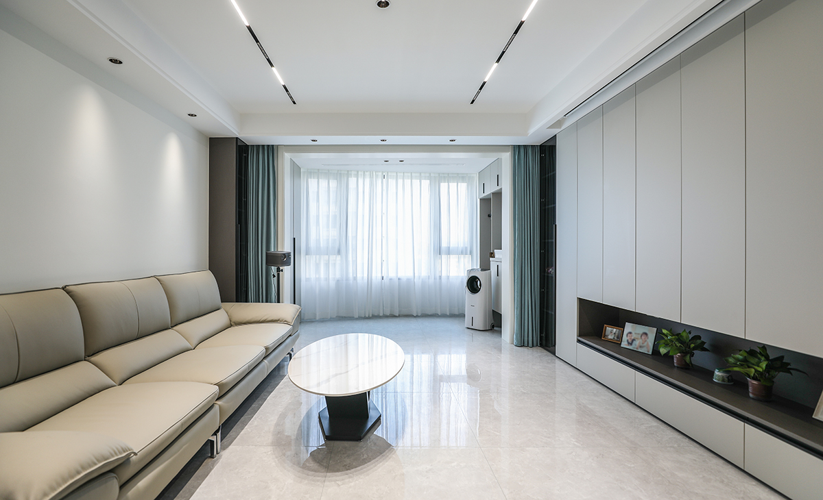 客廳開間很大，滿墻電視柜造型典雅，中間鏤空處理，適當留白，美觀大氣的同時也增加了收納空間。米灰色沙發(fā)遙相呼應(yīng)，整體和諧統(tǒng)一，將空間感拉伸的更加開闊。吊頂造型上采用滿頂無主燈吊頂。地面采用淺灰色地磚。造型和色調(diào)上簡潔，明快，給人以一種現(xiàn)代感十足的高雅感受。