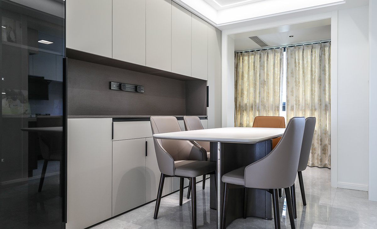 餐廳區(qū)域戶型周正，緊鄰小陽臺，空間通透采光好，沿墻滿做一排餐邊柜，實用且高級，增加儲物功能的同時，更為裝飾效果加分，嵌在餐邊柜上的移動排插也解決了客戶的用電剛需，整體色彩以黑白灰為主，造型美觀大氣。