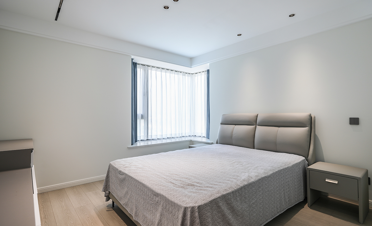 主臥地面鋪以暖灰色地板，衣柜與墻面色彩統(tǒng)一，相得益彰。四周雙眼皮吊頂加上中間拉平無主燈的設(shè)計，讓空間顯得尤為寬敞，灰色的床及床頭柜與整個風格進行搭配，渾然一體，整體協(xié)調(diào)，盡顯主人高端品味。