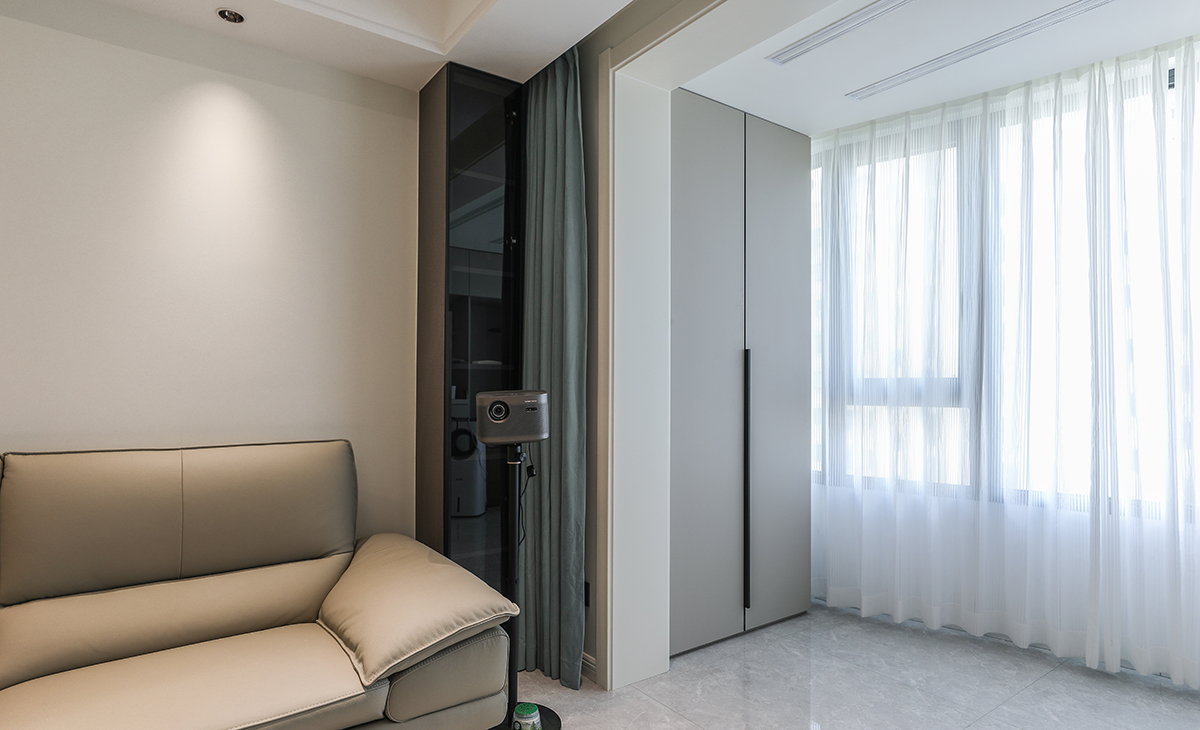 陽臺的頂部暗藏隱形晾衣架，石膏板吊頂之后，頂面平整有序。洗衣機的對面一側(cè)，采取全屋定制儲物柜，選用灰色門板加黑色長拉手，一門到頂，整齊又好看。