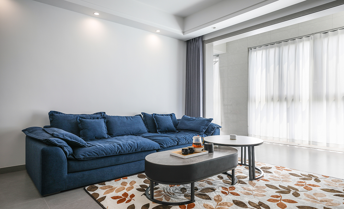 沙發背景刷淺灰色涂料，白色的沙簾，沙發背景留白設計，色調上墻面涂料和窗簾用淺色，沙發用深藍色，深淺搭配的錯落有致，既溫馨又簡潔。