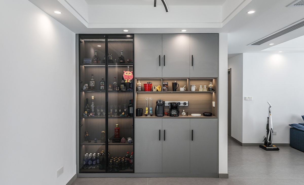 靠著門廳和鞋柜做一排背靠背的餐邊柜，既實用、又有裝飾功能，深灰色框架，極窄邊框玻璃門和淺灰門板相呼應，巖板餐桌把用餐氛圍調和的很溫暖，淺灰色柔光地磚很干凈，色彩和造型上都簡潔大氣。