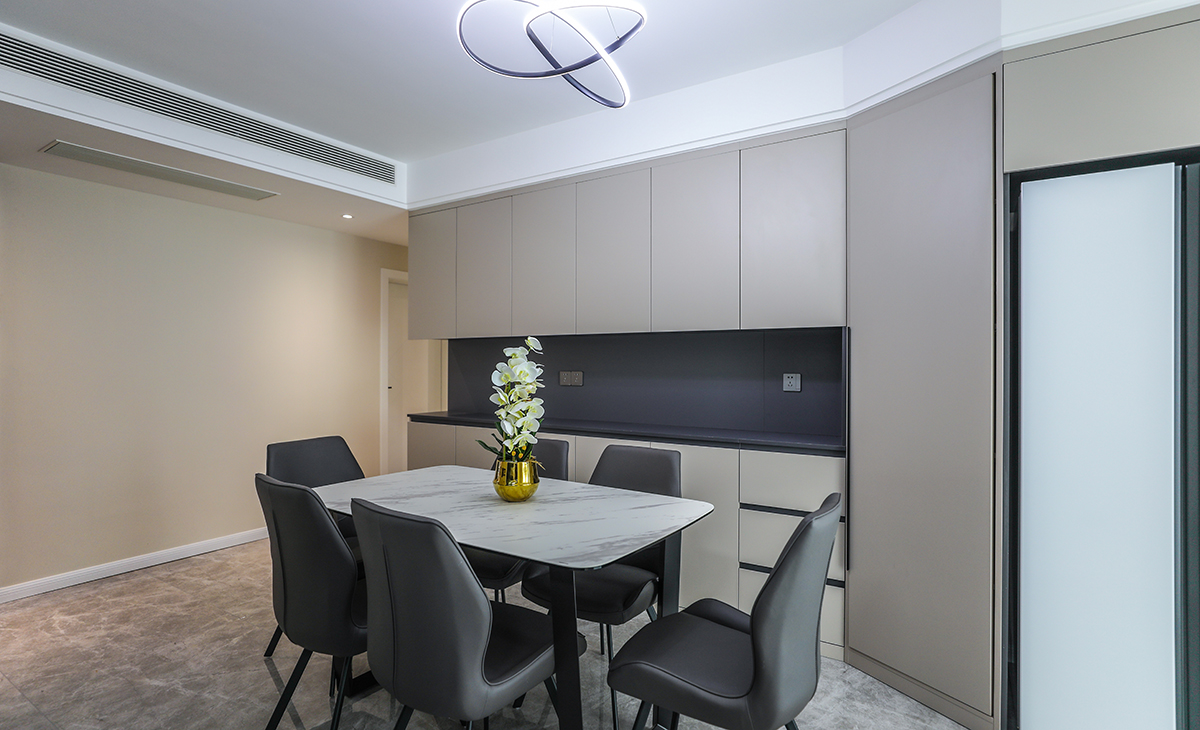 餐廳的餐邊柜加上雙門大冰箱一體合成，灰色柜體板和瓷磚呼應，奶咖色柜門板讓整個家庭溫馨起來，超薄巖板餐桌簡約大氣。