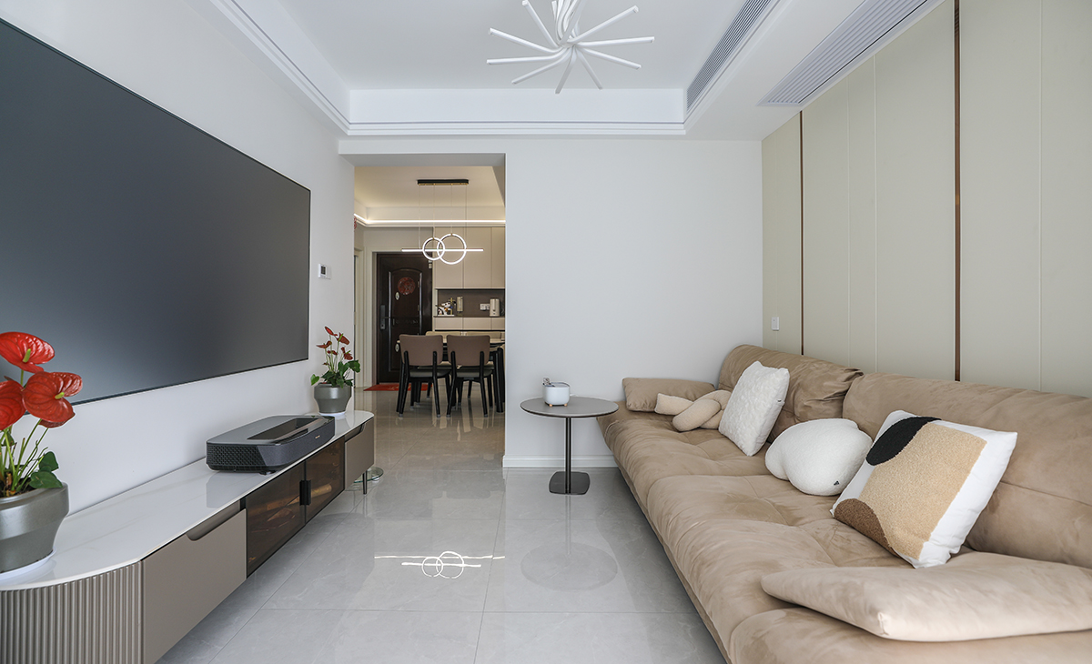 客廳開間并不大，電視墻也并不是很長，所以對于電視墻沒有做過多的裝飾，后期配上65寸的激光電視更顯簡約。暖色調一字型布藝沙發給冰冷的空間帶來一絲溫暖，吊頂造型上采用雙眼皮吊頂下邊沿嵌入線條燈，增加房屋的層次以及氛圍感。地面采用淺灰色地磚。造型和色調上無不給人以簡潔、大氣、時尚的感覺。