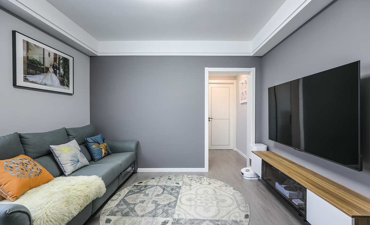 整個客廳以簡約為主，主要由于客廳空間布局并不富裕，空間感通過不同灰度拉開層次，并且在局部運用了亮色作為點綴豐富場景，比如沙發上的抱枕，電視柜的木飾面，地板同樣采用灰色系，搭配地毯的材質對比，增加空間的樂趣。
   餐邊柜整體原木色搭配奶白色門板，依然主打簡約，搭配巖板的餐桌，