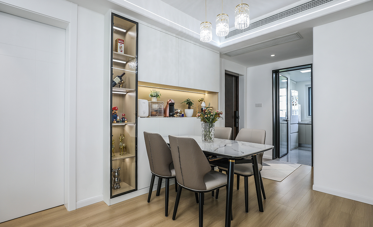 餐廳空間比較方正寬敞，靠墻做一排裝飾柜，既實用、又有裝飾功能，原木色框架，極窄邊框玻璃門和白色木門板相呼應，巖板餐桌把用餐氛圍調和的很溫暖，原木色地板很干凈，色彩和造型上都簡潔大氣。