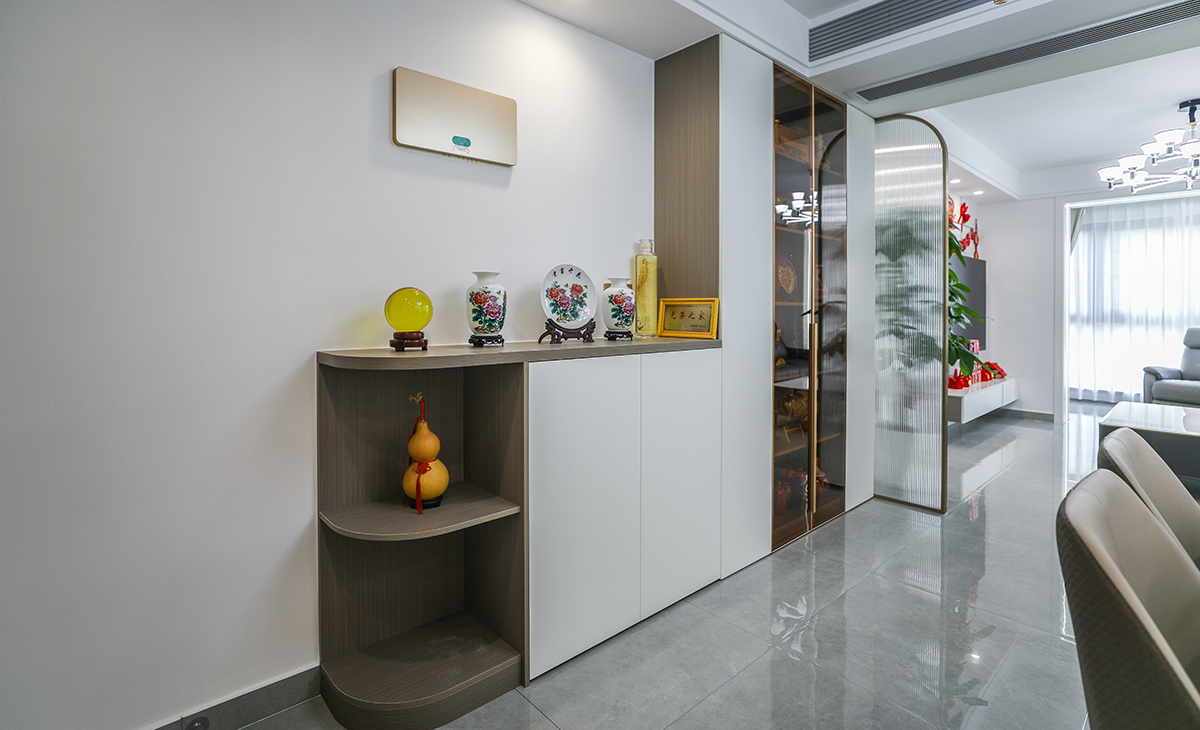 本套房子的進門玄關柜設計也是一大亮點，對外圓弧形角矮柜到內頂天立地四扇高柜，中間玻璃門，體現了主人生意人的處事圓潤，做人挺直腰桿心胸坦蕩，屏風采用金色弧形設計，和矮柜圓形角相呼應，給人感覺不僅雅致而且有韻味。