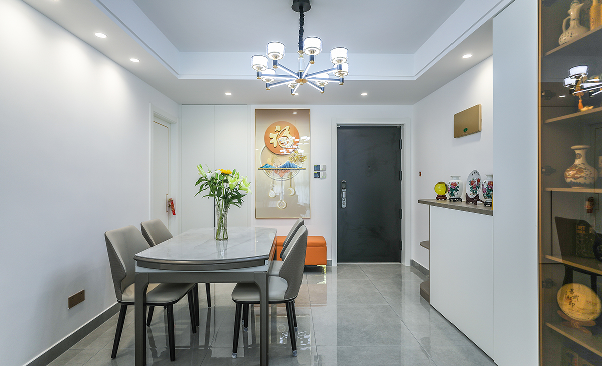 餐廳空間比較方正寬敞，進門右手邊是橙色換鞋凳，和裝飾畫遙相呼應，靠左墻做一排矮柜和酒柜，既實用、又有裝飾功能，原木色框架，極窄邊框玻璃門和白色木門板相呼應，巖板餐桌把用餐氛圍調和的很溫暖，淺灰色地磚很干凈，色彩和造型上都簡潔大氣。