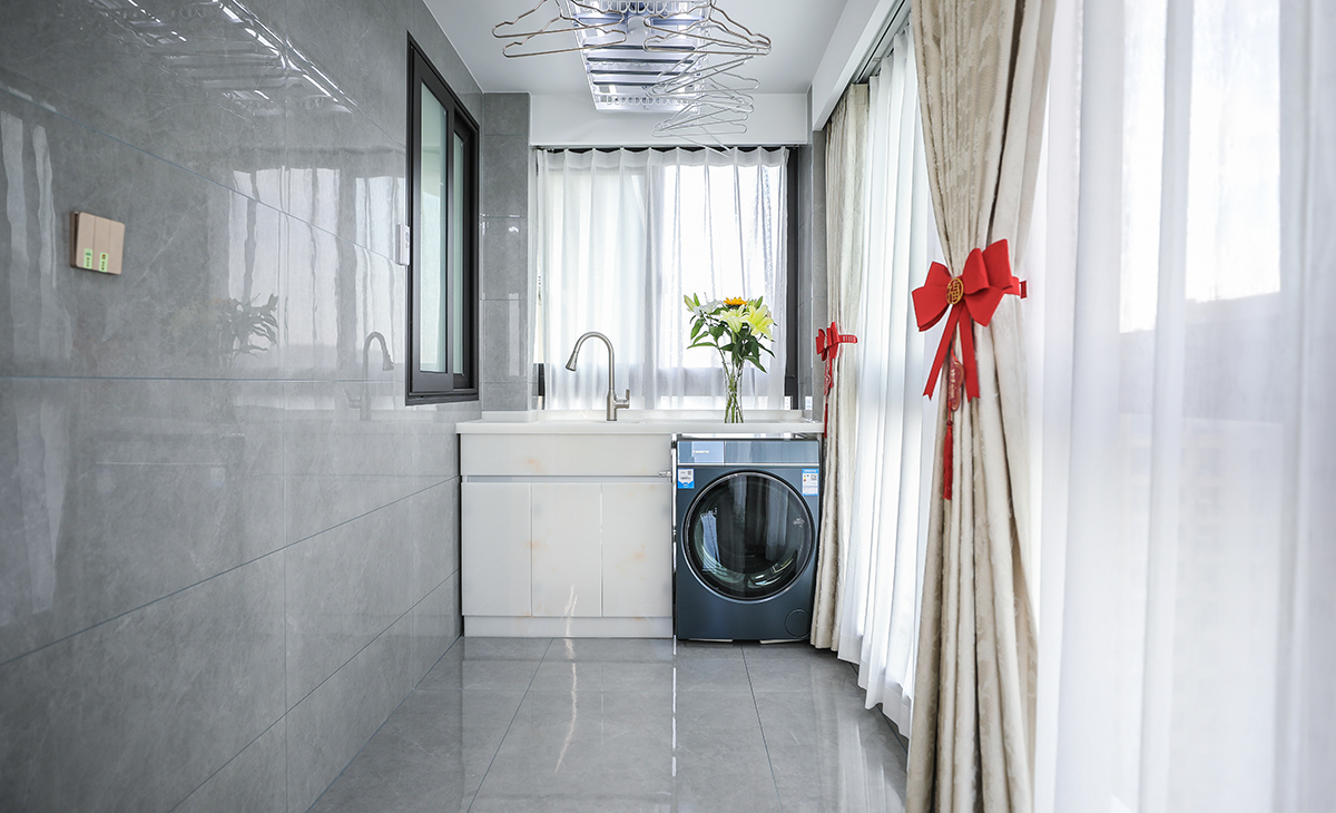 陽臺是晾曬衣物的場所，一側洗衣機和水池，一側為按摩椅，顏色以灰色為主，超大落地玻璃窗讓陽光柔和的照進來，很舒適、很愜意。