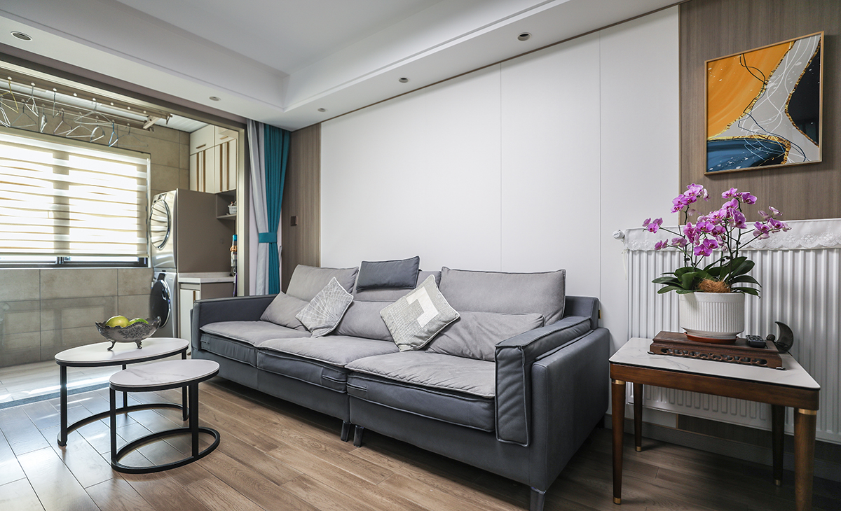 沙發(fā)背景墻也是采用纖維大板材質(zhì)，用純色和木色進(jìn)行簡單拼接，沙發(fā)邊放上一個邊幾，放置裝飾花瓶和掛畫，作為點(diǎn)綴，讓整個空間變得更加靈動。