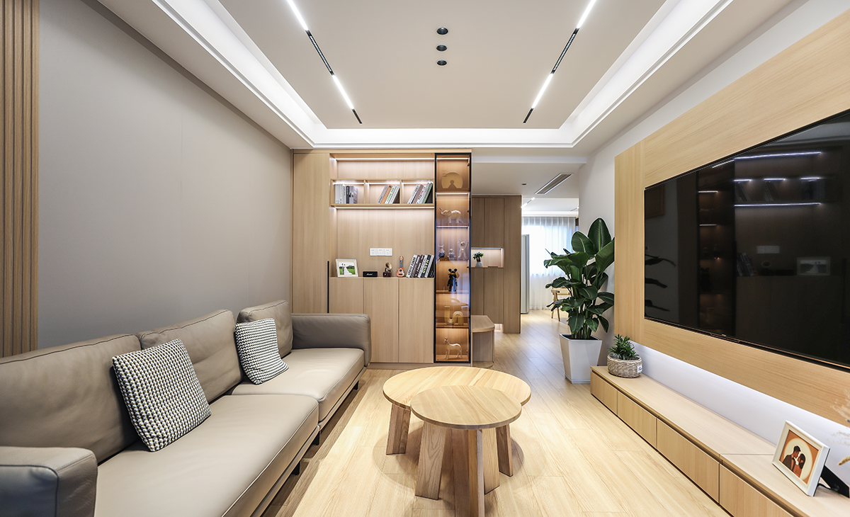 沙發邊上正好放一個收納柜，原木色的柜體、門板配色黑色玻璃，簡約又時尚，顏色統一，整體安裝線性燈拉長，空間感更時尚、大氣。