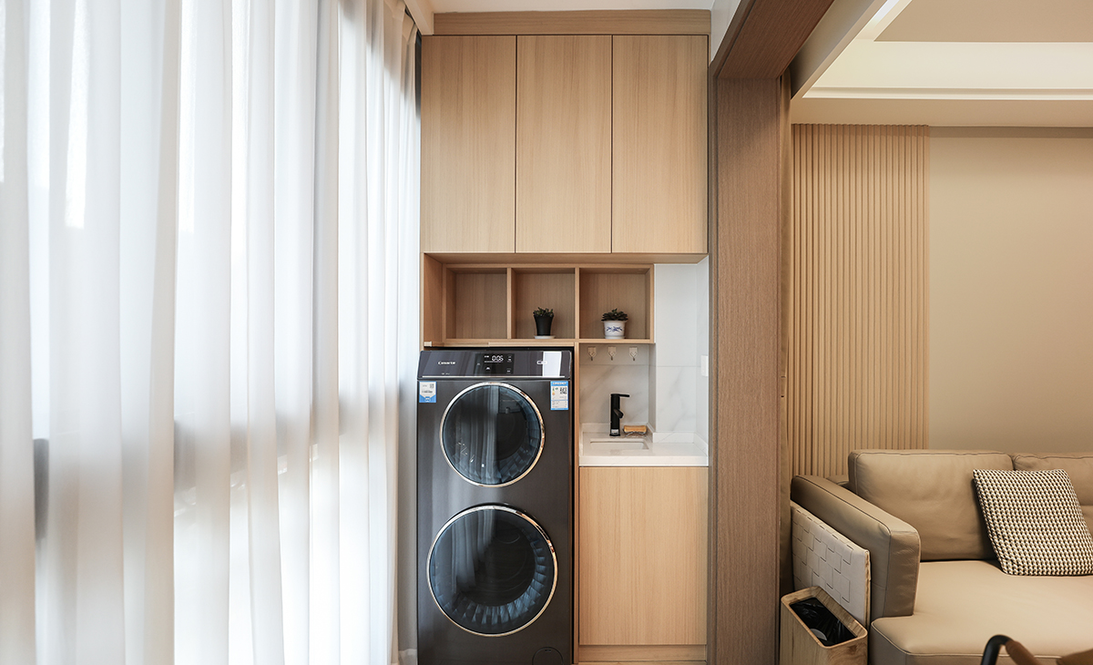 陽臺作為生活的晾曬衣物場所，它不僅有收納和洗衣服功能，整體空間設計好以后，效果更突出，也能作為觀賞的一處景物。原木色柜體和門板做了當下很流行的洗衣柜組合，上面的收納柜和對面的儲物柜形成了鮮明的對比，長長的收納柜，既可以放吸塵器，又美觀簡約時尚，配上白色紗簾，把原木色的風格，簡單明了的凸顯出來，既時尚又溫馨，達到了業主想要的美觀和實用并存的效果。