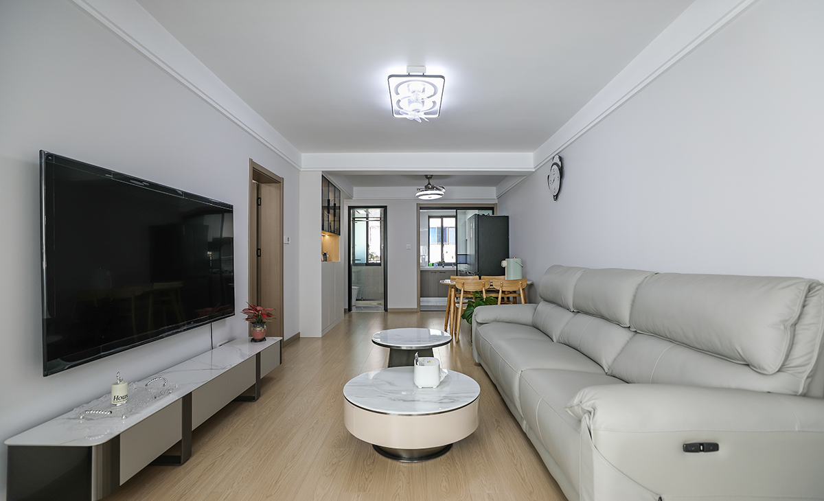 客廳開間很大，淺灰色皮質沙發立刻檔次提高很多，網紅茶幾，客廳空間也很寬闊。吊頂造型上采用雙眼皮吊頂。地面采用原木色地板。造型和色調上無不給人以簡潔、時尚的感覺。