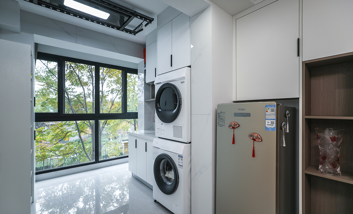 陽臺是晾曬衣物的場所，洗衣機和烘干機疊放旁邊放水槽，上方為儲物柜，顏色以米白色為主大玻璃窗讓陽光柔和的照進來，很舒適、很愜意。