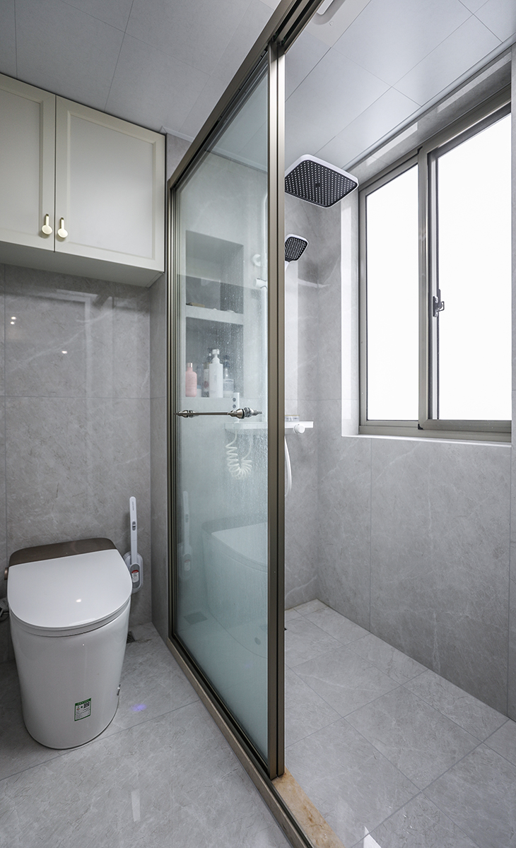 衛(wèi)生間做干濕分開，淋浴區(qū)利于原有管道做壁龕增加儲物的同時合理利用每一份空間，馬桶上增加儲物柜，增加收納空間，金色窄框淋浴房，線條簡單，墻地面通鋪一體大磚，單獨淋浴區(qū)同色小磚做下水坡度。讓整個空間協(xié)調(diào)統(tǒng)一，大氣時尚
