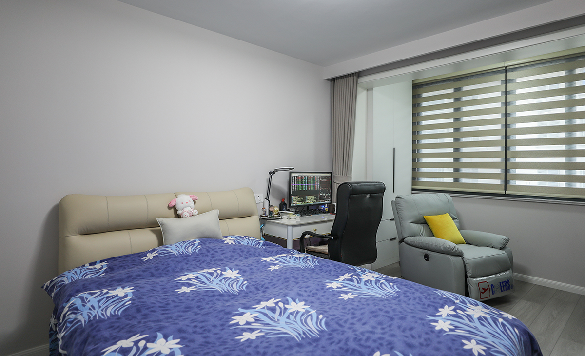 整個臥室的顏色搭配非常協調。床上的被子和毛絨玩具熊是藍白相間的，這種顏色搭配讓人感到寧靜。床頭的顏色是米色，與整個房間的色調非常協調，給人一種溫馨的感覺。墻壁是白色的，這種顏色增加房間的明亮感，讓整個空間更加開闊和舒適。窗戶上安裝了遮光簾，阻擋陽光的直射，同時也可以讓室內保持舒適的溫度。整個房間的顏色搭配非常協調，給人一種溫馨舒適的感覺。