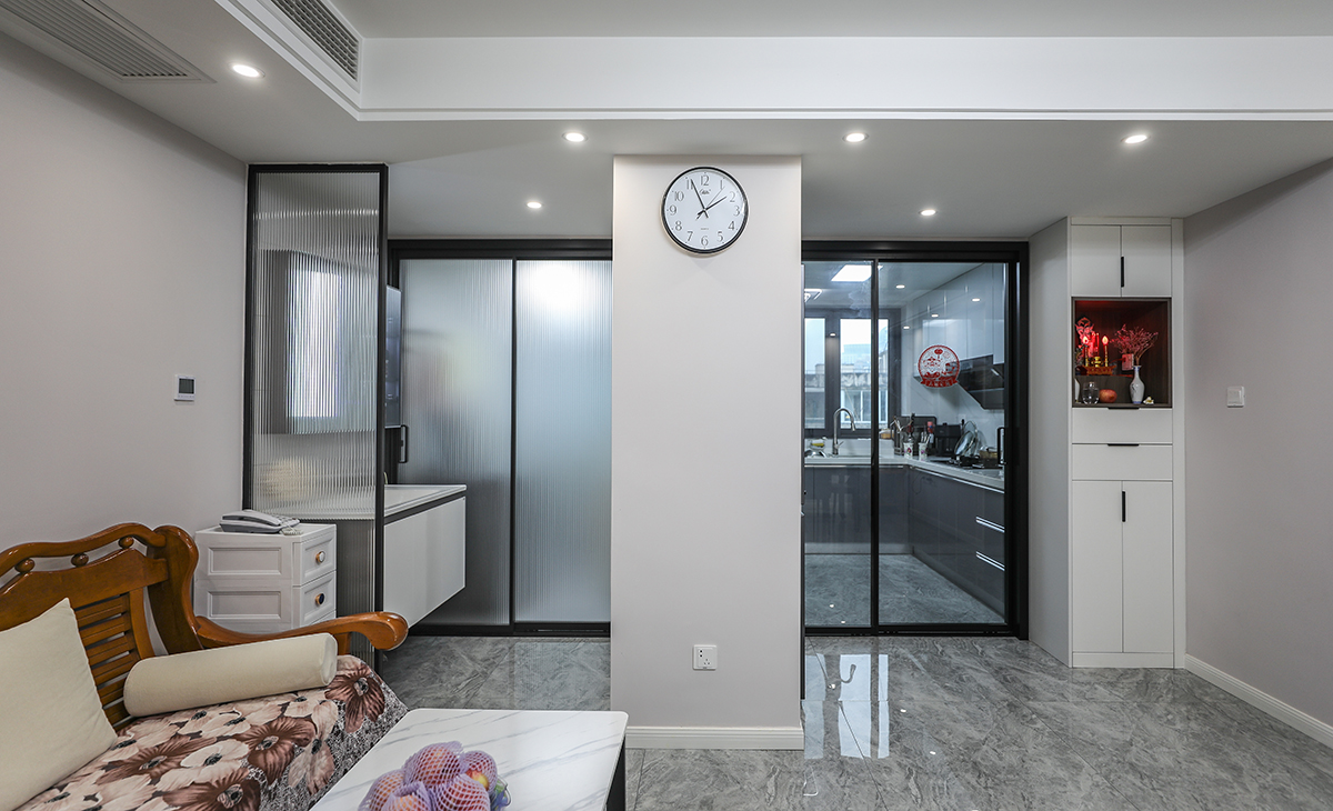 廚房和客廳的隔斷非常獨特。通過玻璃門作為隔斷，客廳內的物品和廚房的烹飪活動可以相互展現，增加了空間的通透感。沙發和桌子是客廳的基本家具，為人們提供休息和工作的空間。而那個時鐘則提醒我們珍惜時間，同時給整個空間增添了一份溫馨的氛圍。