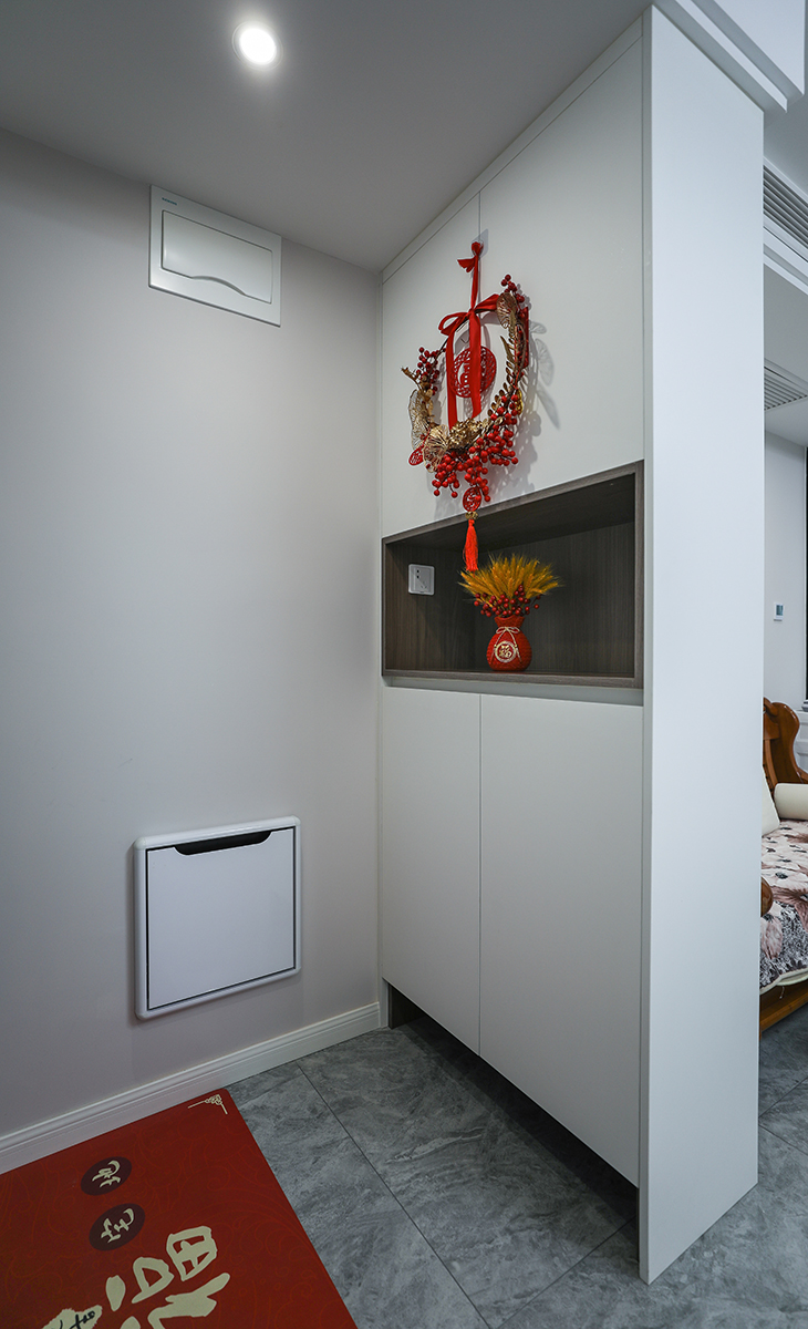 玄關柜功能上在接待客人、換衣、換鞋和放包的功能等，還具有延伸空間的效果。此外，它也可以打造成小平臺，放置小物品如鑰匙，從而增加居家裝飾的趣味性。中國結和裝飾品則懸掛在柜子的上方，這種布局方式不僅突出了紅色元素，還增加了空間的藝術感和層次感玄關在視覺上起到屏障作用，避免開門即看到客廳內部，確保私密性和距離感，特別在家人或朋友來訪時，能有效解決視覺干擾和心理安全問題，使出入過程更加有序。