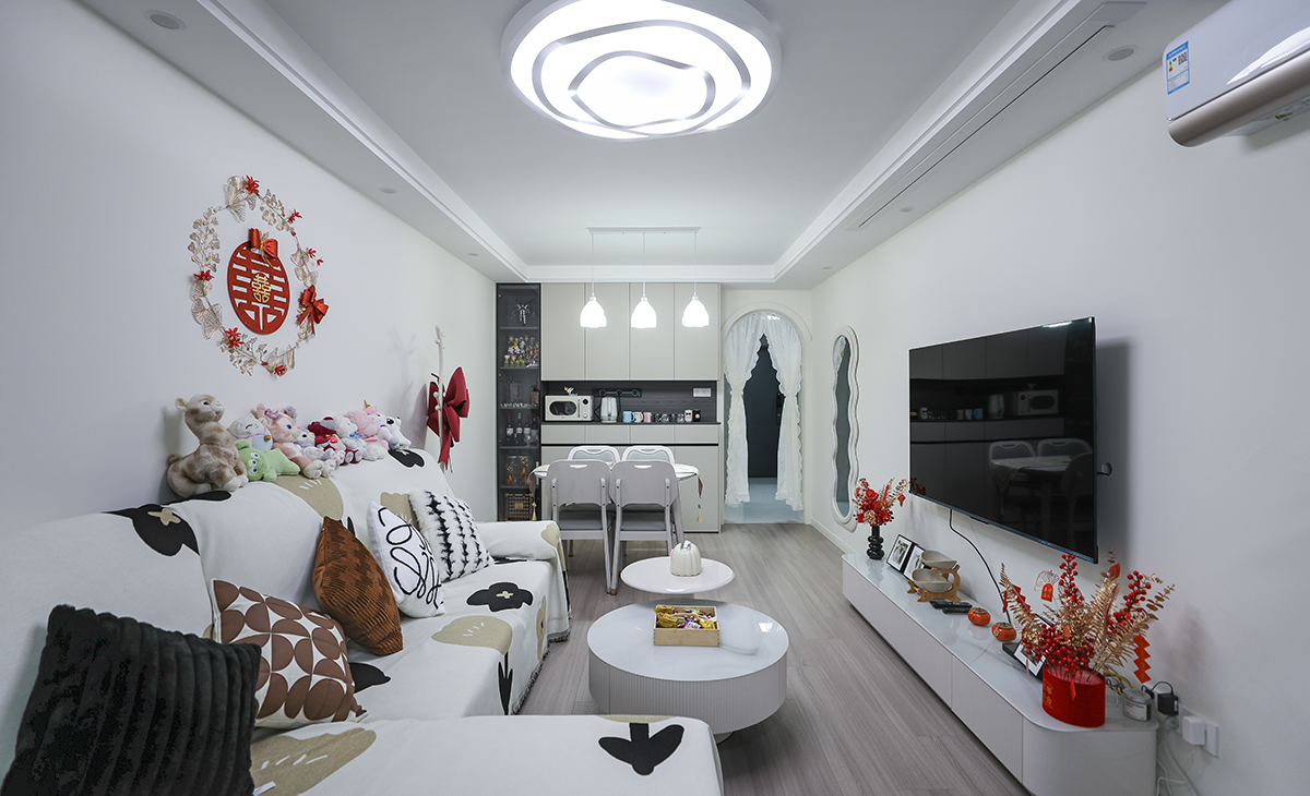 客廳開間較長，平時用電視機，周末休息時可以用投影在家里就能體驗影院般的效果，空間也很寬闊、裝飾柜采用淺灰色門板，墻面用暖白涂料增加亮度，吊頂造型上采用雙眼皮吊頂。地面采用淺灰木色地板。造型和色調上無不給人以簡潔、大氣、時尚的感覺。