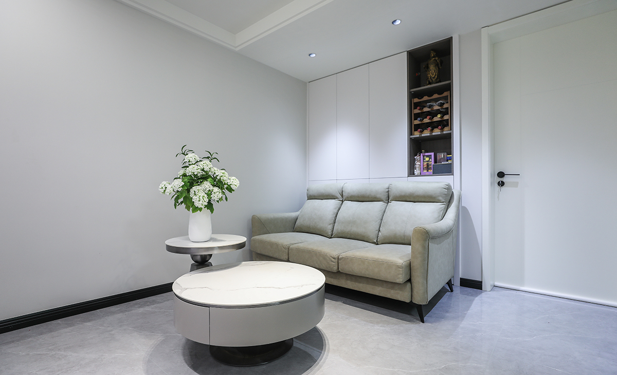 沙發(fā)背景上吊嵌入式壁柜，白色的門板配備深灰色開放隔顏色相輔相成，因客戶家為一樓光線較暗，色調(diào)上墻面涂料全部采用白色乳膠漆，沙發(fā)用淺灰色，深淺搭配的錯(cuò)落有致，既溫馨又簡(jiǎn)潔。