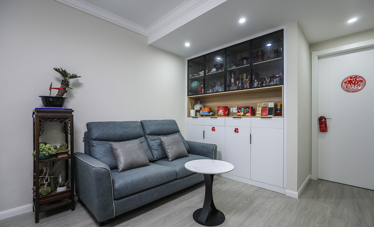 沙發背景刷淺灰色涂料，邊柜亦采用了乳白色門板搭配原木色底板，上柜采用了深色玻璃柜，色調上墻面涂料用淺色，沙發用深色，深淺搭配的錯落有致，既溫馨又簡潔。