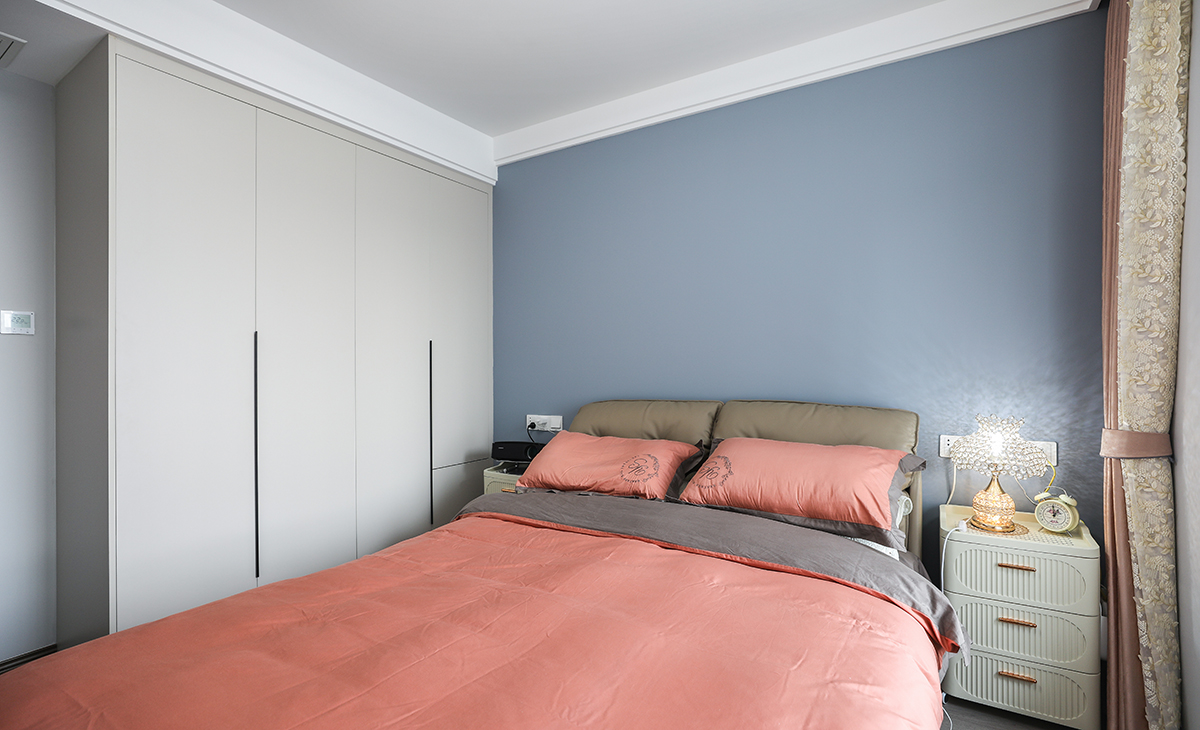 整個臥室看起來非常舒適和溫馨。白色墻壁和灰色地板給人一種寧靜的感覺，而床上用品的顏色則增添了一些活力和溫暖。棕色門和黑色杯子則提供了對比和質感。家具的布局也很合理，提供了足夠的儲物空間和舒適的休息區域。