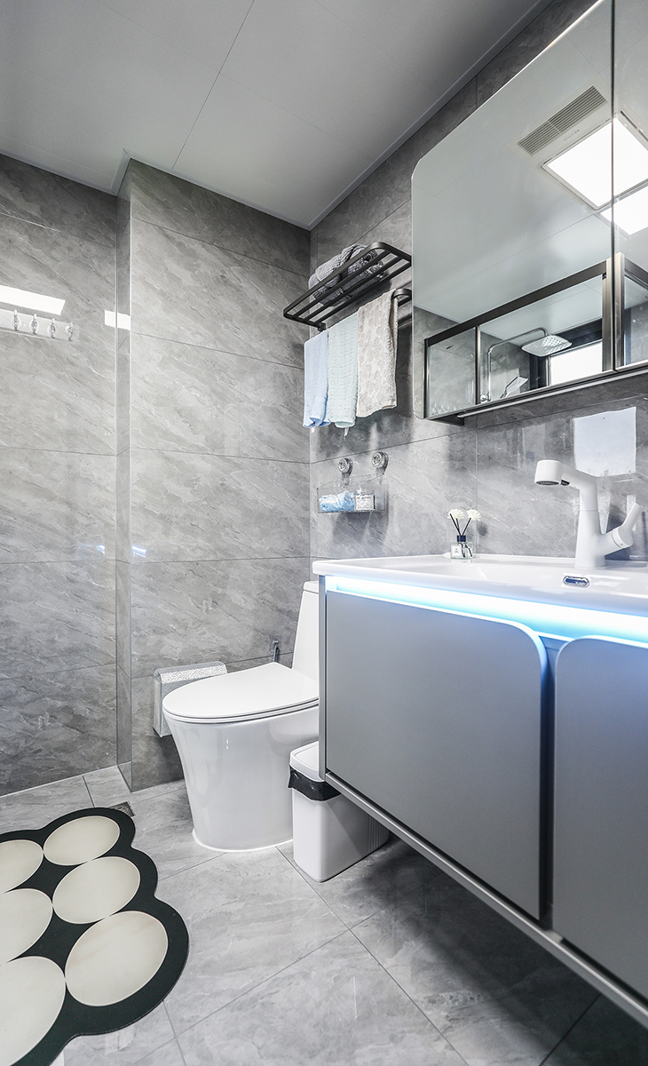 衛生間設計風格簡約而時尚，整體色調以白色和灰色為主，給人一種清新整潔的感覺。墻磚采用淺灰色，與白色馬桶相得益彰，而洗手臺上的一條燈帶更加的增強了空間的層次感。