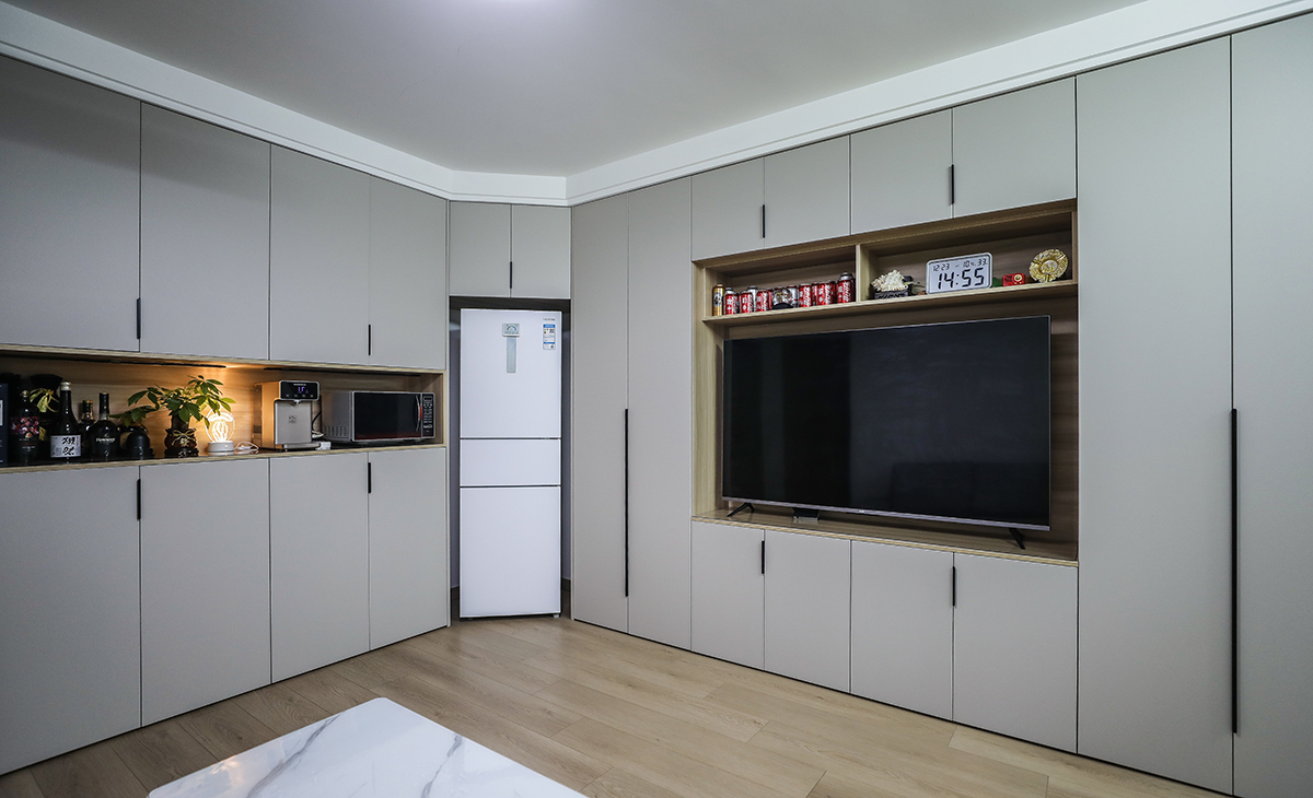  本套房子的客廳儲物柜設計是一大亮點，既實用，又有裝飾性，上下儲物柜，中間留鏤空，展示主人收藏的藝術品，門板采用平板一門到頂，和臥室門顏色相統一，給人感覺不僅雅致而且有韻味。