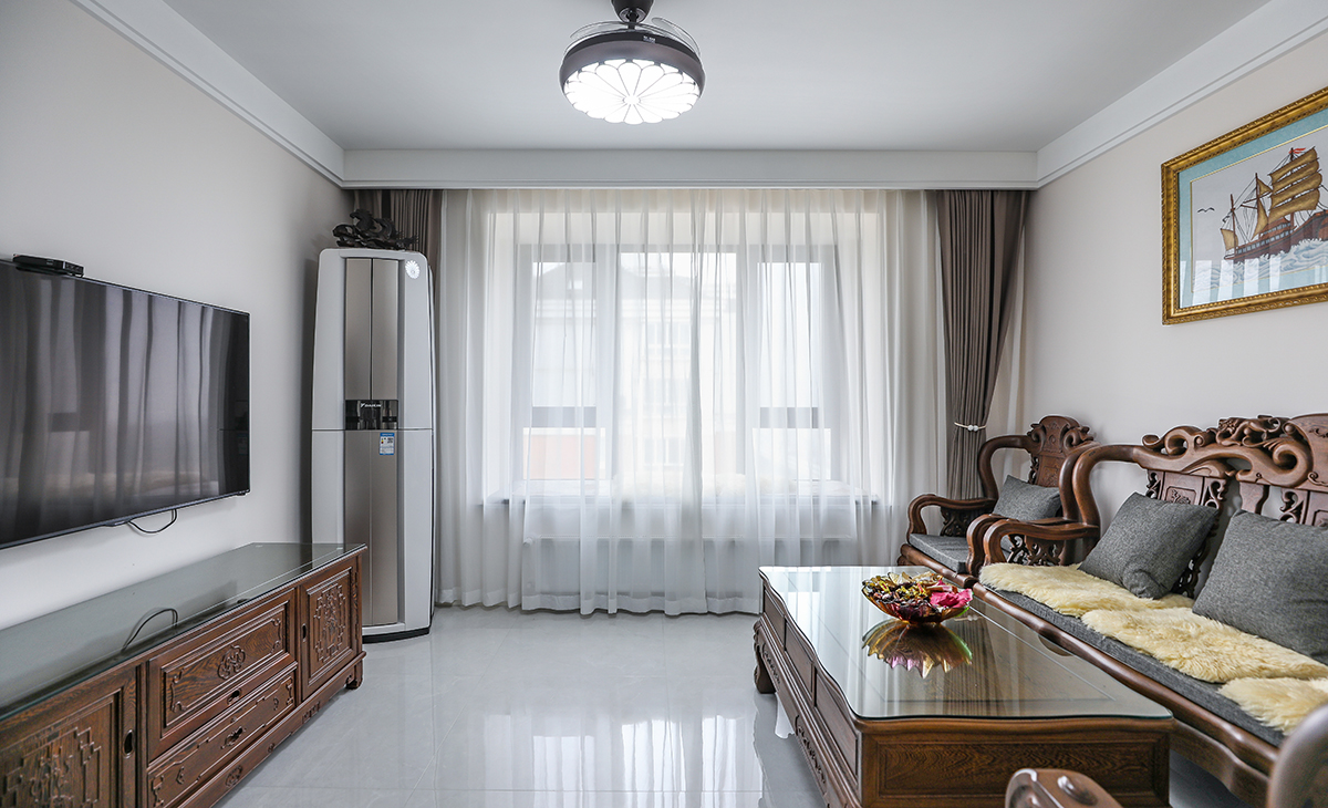  客廳開間很大，客戶家里實木家具是原先保留下來的，雞翅木質感強硬，跟客戶雍容華貴的身份相吻合?？蛷d空間也很寬闊。吊頂造型上采用雙眼皮吊頂。地面采用淺灰色地磚。造型和色調上無不給人以簡潔、大氣、時尚的感覺。