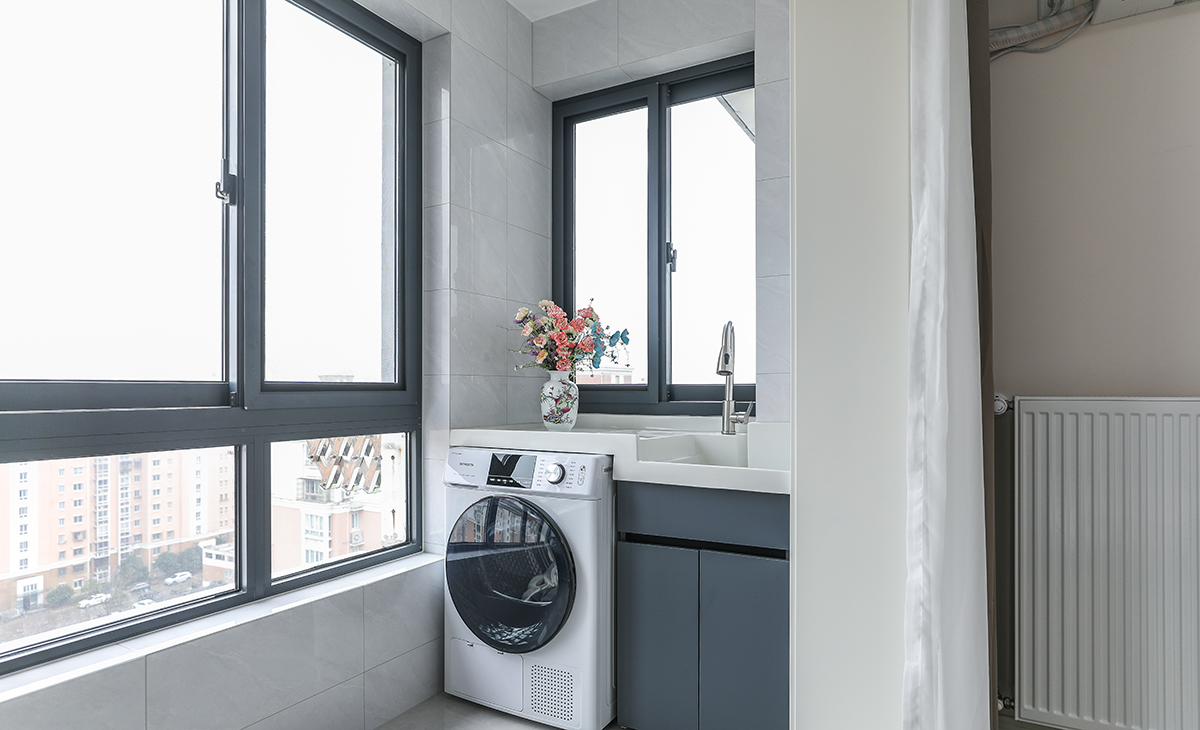 陽臺是晾曬衣物的場所，一側烘干機和水池，一側為儲物柜，顏色以白色為主，儲物柜白色門板和門套相搭配，超大玻璃窗讓陽光柔和的照進來，很舒適、很愜意。