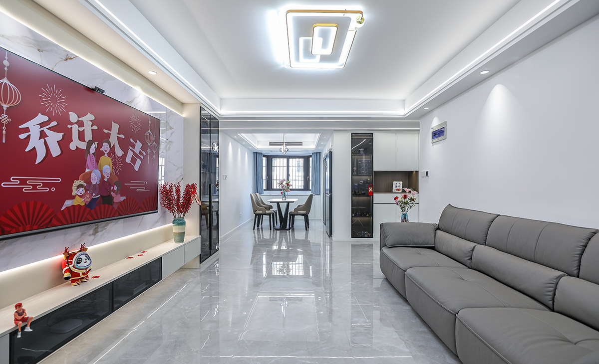  客廳開(kāi)間很大，電視墻做了巖板與木飾格柵，淺的巖板和原木色木飾面相互配合，明暗有神，深灰色皮質(zhì)沙發(fā)立刻檔次提高很多，客廳空間也很寬闊。吊頂造型上采用雙眼皮加線性燈組合吊頂。地面采用淺灰色地磚。造型和色調(diào)上無(wú)不給人以簡(jiǎn)潔、大氣、時(shí)尚的感覺(jué)。