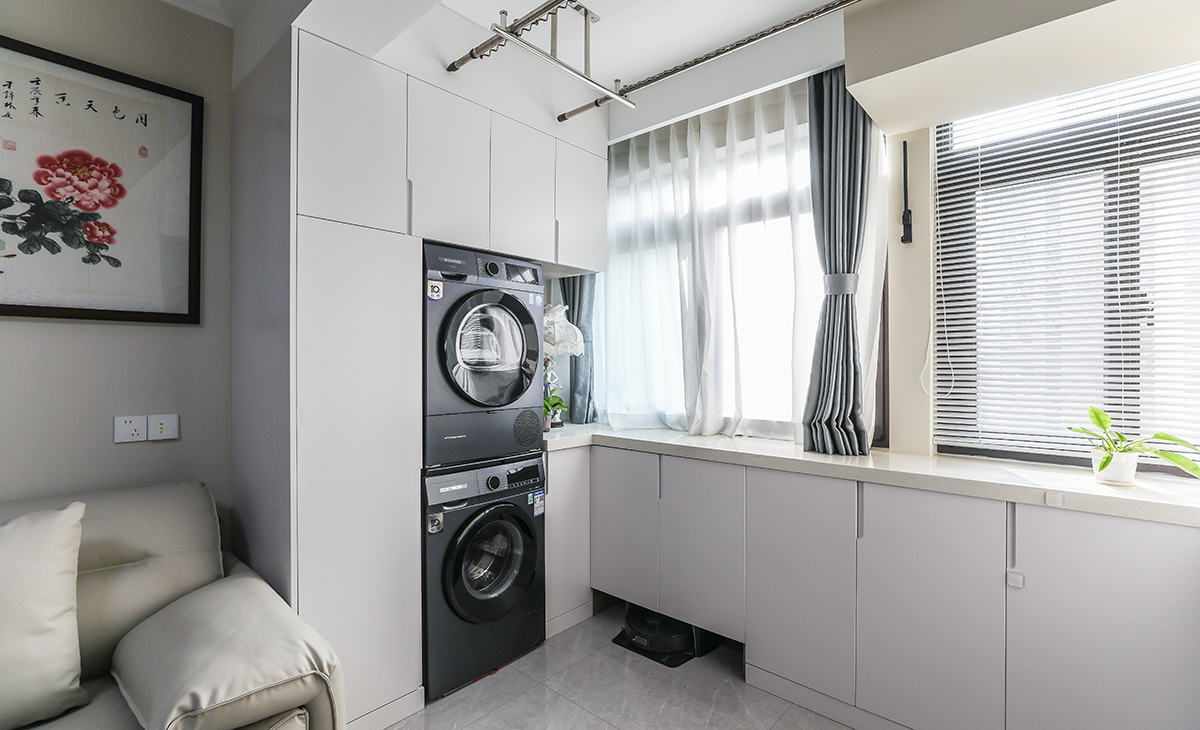 陽(yáng)臺(tái)與客廳打通增大空間的同時(shí)也做了大量的儲(chǔ)物，洗衣機(jī)烘干機(jī)上下疊放，邊上做了一組家政柜放置吸塵器等家政用品，小小的空間有大大的利用。