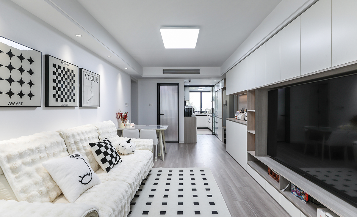 客廳面積不大，但經過設計師的手筆，讓空間緊湊不擁擠，電視墻做成整面定制柜和鏤空柜相結合，既增加儲物有不顯單調、擁擠，灰色柜體和地板相呼應，啞白色門板簡單、大氣，白絨沙發搭配地毯立刻檔次提高很多。吊頂造型上采用雙眼皮吊頂，時尚又大氣。地面采用淺灰色木紋地板。造型和色調上無不給人以簡潔、大氣、時尚的感覺。