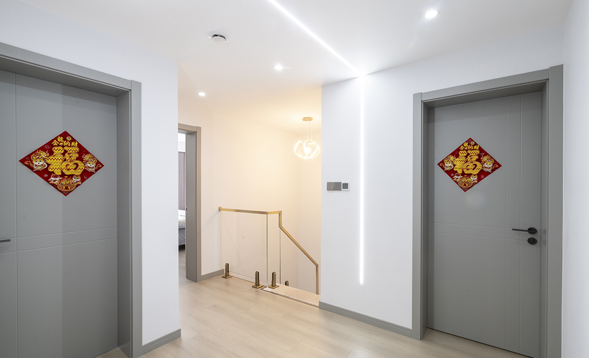 樓梯上來就是休閑區，采用無主燈設計，墻面和頂面的倒U字型線燈，讓空間豐富起來，白色墻面和灰色木門搭配，光線明亮通透，顏色搭配明暗有序。