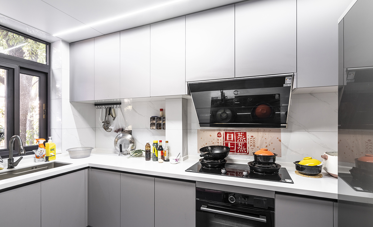 該套房子廚房空間很大，做成L型櫥柜，蒸烤一體機放煤氣灶下面，上柜淺灰、下柜深灰，臺面白色，方便打理，大雙門冰箱滿足儲物空間。