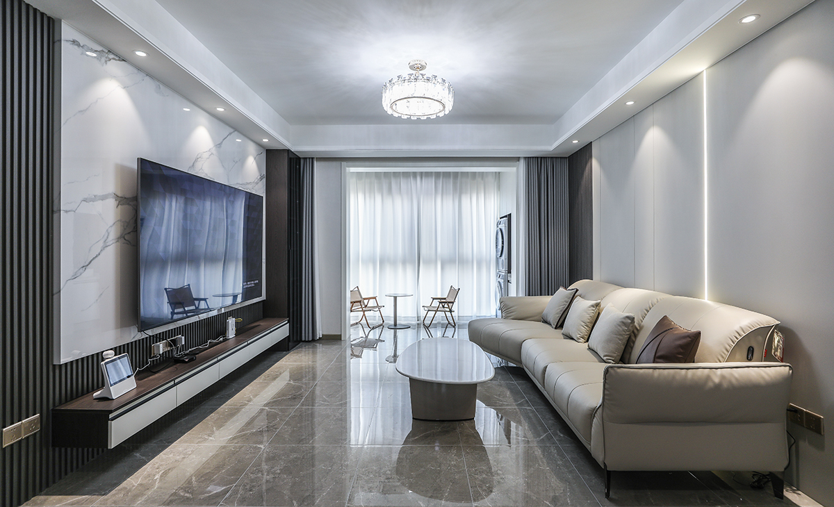 客廳開間很大，電視墻做兩片巖板，兩塊木飾面，淺的巖板和原木色木飾面相互配合，明暗有神，深灰色皮質沙發立刻檔次提高很多，放一組貴妃沙發，客廳空間也很寬闊。吊頂造型上采用雙眼皮吊頂。地面采用淺灰色地磚。造型和色調上無不給人以簡潔、大氣、時尚的感覺。