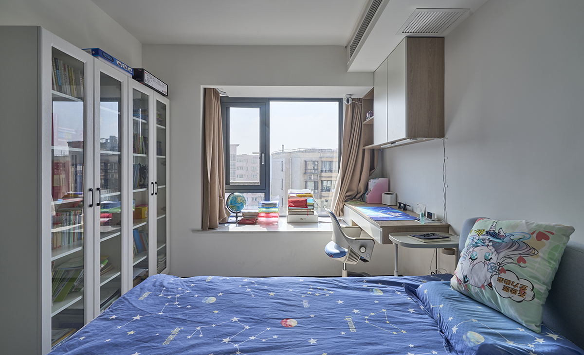 兒子房也有大飄窗，利用飄窗做一個懸挑寫字臺，上面吊柜，寫字臺對面又有一排書柜，有效收納了兒子的書籍。