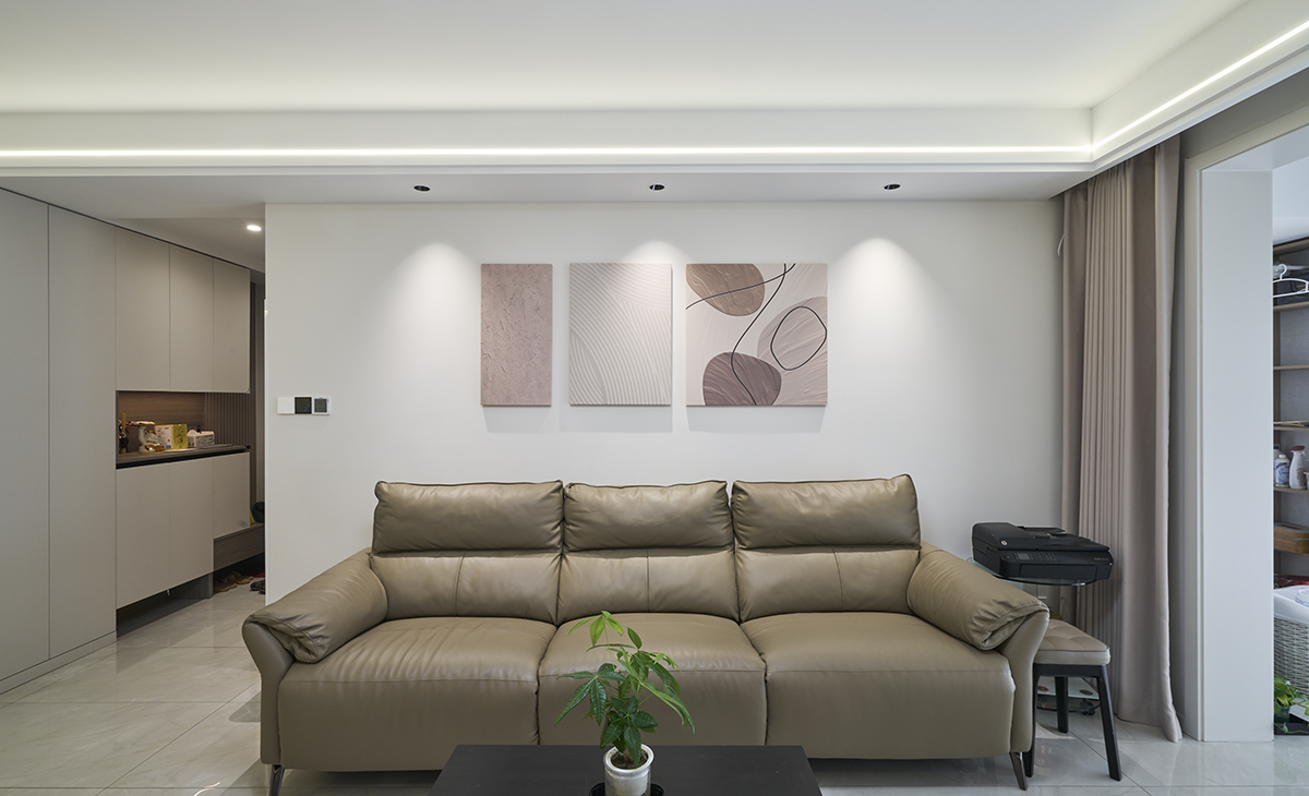 沙發背景墻上3副大小不一的掛畫，盡顯活潑生動，頂上三個射燈點綴的恰到好處，讓客廳整個空間感覺簡潔清爽。