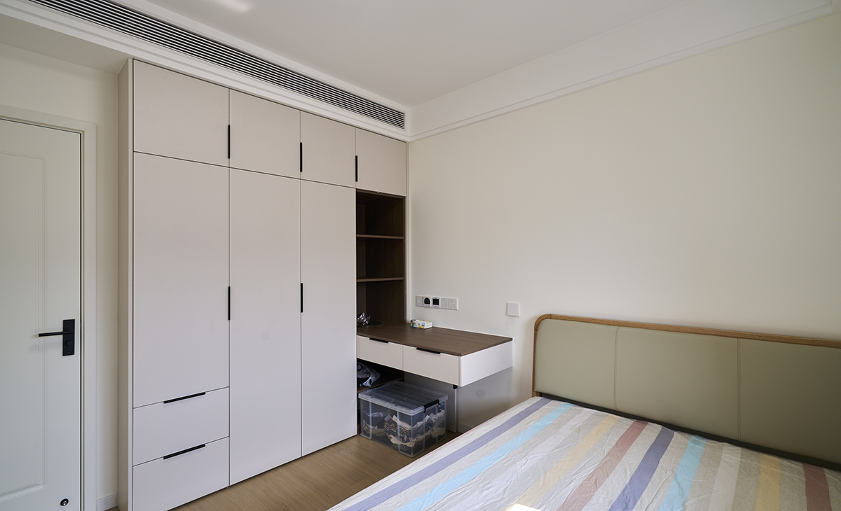 次臥空間不大，衣柜延伸出梳妝臺，梳妝臺下方可以放行李架，原木色的地板，淺灰色踢腳板，配白色墻面，顏色明暗對比有序。