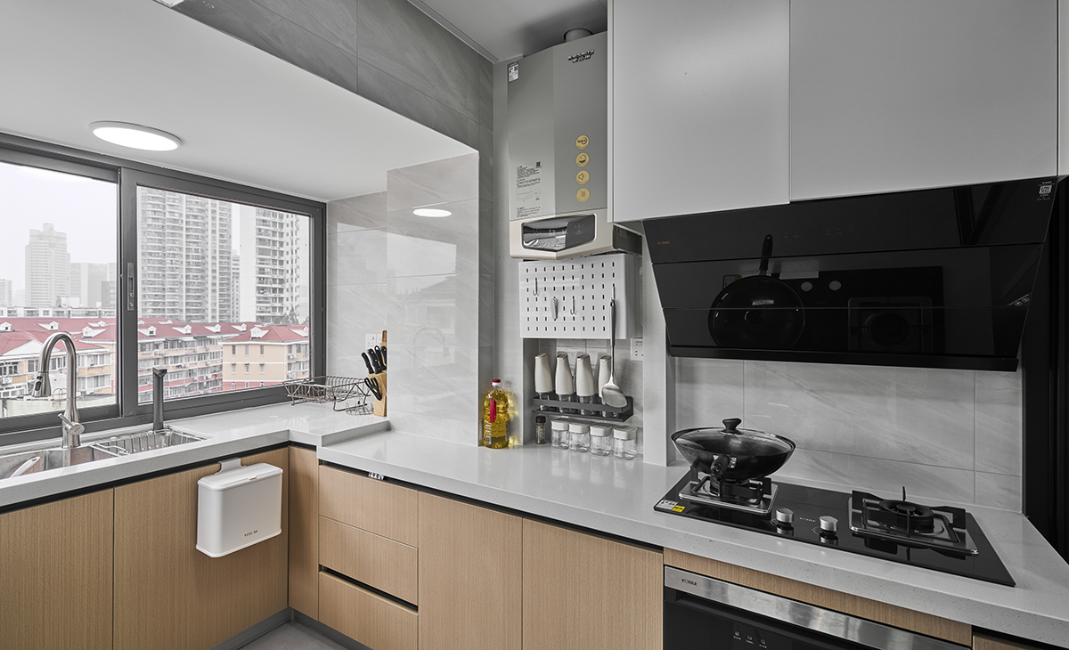 該套房子廚房空間很大，臺面做成高低臺面，熱水器明裝，煤氣灶下方配消毒柜，上柜是白色，下柜是原木色，臺面白色，方便打理，墻地磚的顏色和櫥柜顏色搭配地很自然，客戶不斷地夸贊設計師對色彩的精準把握。