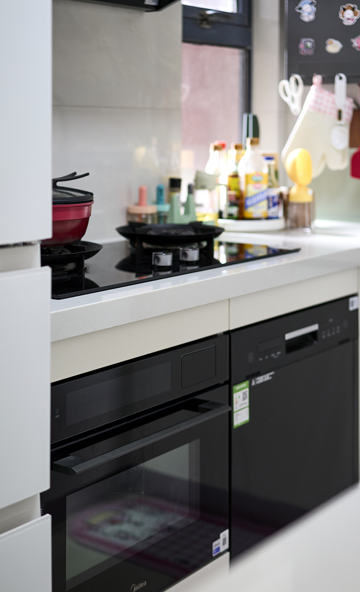 該套房子廚房是開放式，做成U字型櫥柜，煤氣灶下方配洗碗機和蒸烤箱，上柜下柜儲物空間滿滿當當，臺面巖板，方便打理，墻地磚的顏色和櫥柜顏色搭配地很自然，客戶不斷地夸贊設計師對色彩的精準把握。