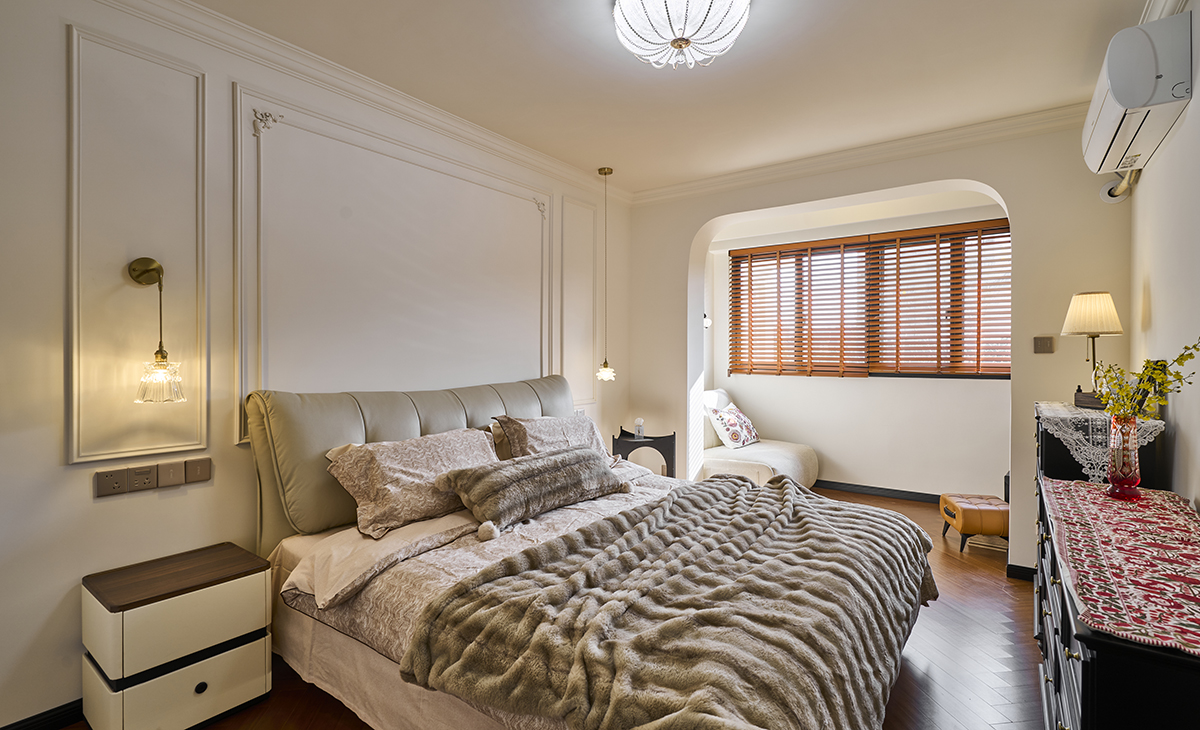 主臥床尾拱形門洞連接白色單人沙發與木質邊幾，木質百葉窗過濾自然光，營造半私密休憩區。