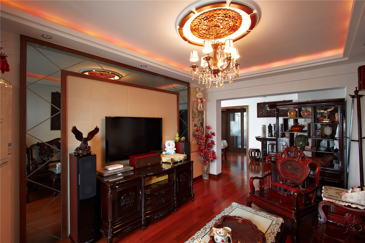 由于客廳不是很寬，且客戶配備的是色系較深的中式家具，使得原本狹小的空間更加擁擠，于是在背景墻采用了米色皮紋磚與灰鏡相結合，灰鏡使得狹窄的空間變得寬。米色的皮紋磚更加襯托了家具的質感，木線條的色系與家具相得易章，協調統一。
