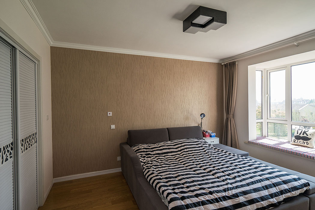 對于臥室來說，黑白兩色過于簡單，所以設計師加入了色澤多樣的軟裝墻紙，盡量使這里體現出溫馨，背景墻咖啡色墻紙與白色的融合，卻富有現代感。