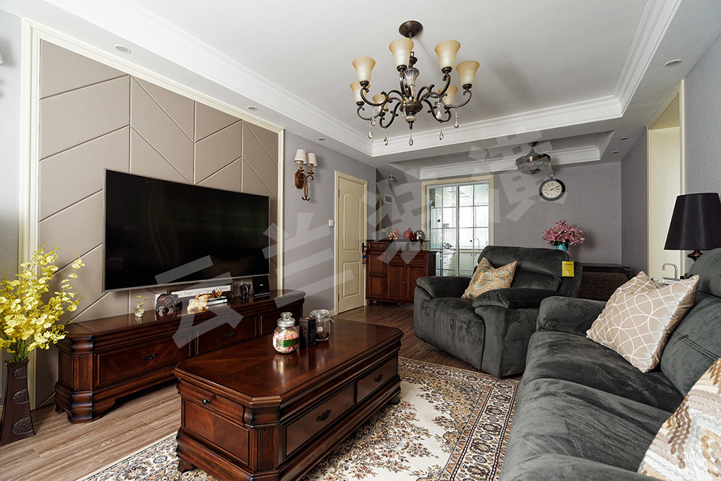 客廳的整體色調和質感偏濃重，作為點睛之筆的電視背景墻，線條明朗的灰色硬包在乳白色木線條的襯托下與沉穩大氣的深色家具相呼應，家具又與藍灰色墻面形成反差，凸顯了客廳的立體感和層次感。
