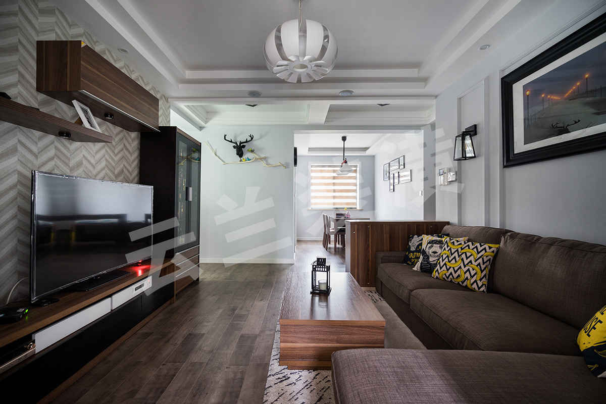  現(xiàn)代人們越來越喜歡簡單化的家具，它舒適更便于打掃，所以客廳的家具雖保持著美式的沉穩(wěn)顏色，但是沒有了繁瑣的花紋和配飾。那更多美式的元素就是藏在與吊頂和立面簡單的畫框線條。他的吊頂更多的是層層疊加，讓整個立面看上去更立體。再配上客戶花心思淘的配飾和掛畫，讓整個空間一下子生動了起來。客廳的整個立面設計都已經簡單化，已有了沙發(fā)背景的線條框，所以電視背景只采用了簡單的墻紙來修飾在配上組合柜來豐富整個格局。最后加上顏色亮麗的掛畫和抱枕讓整體空間都生機勃勃了起來。

